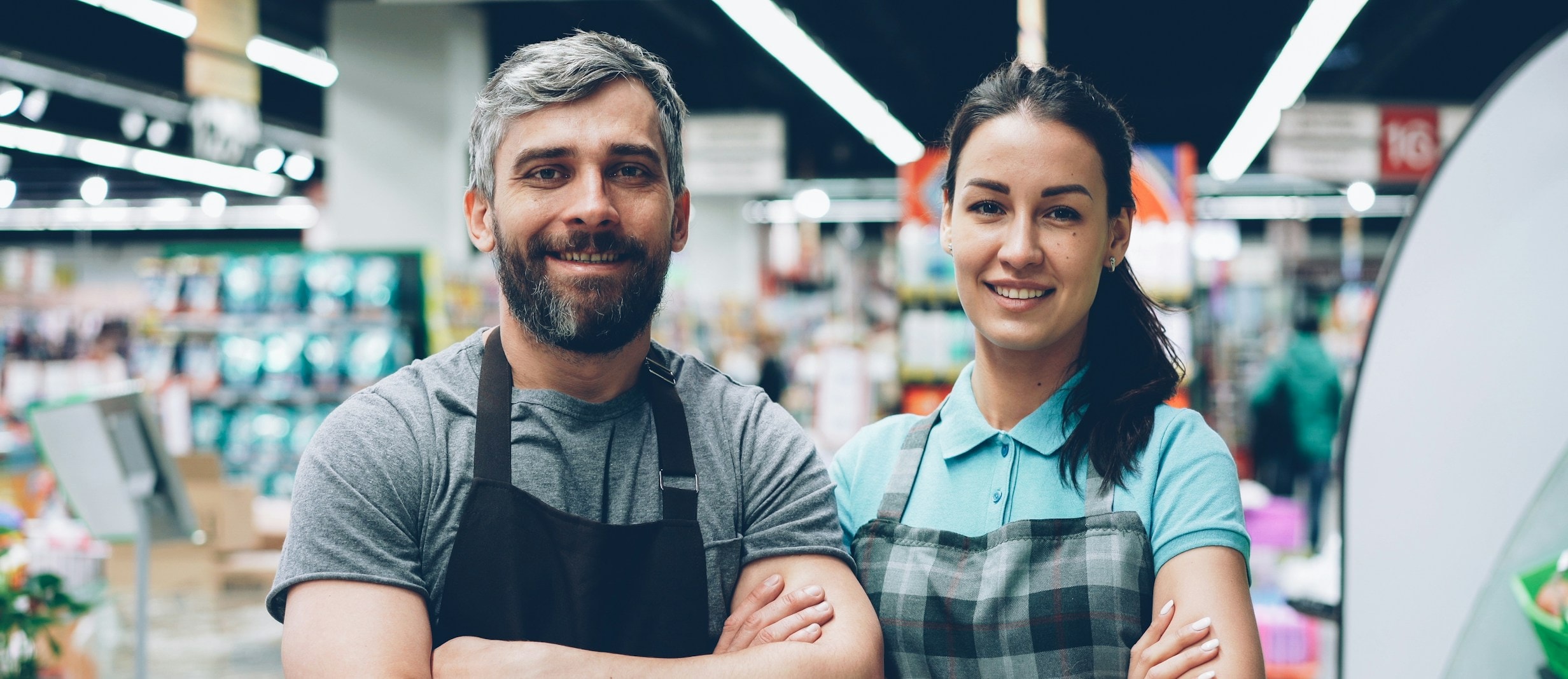 Dos personas que atienden un almacén, de brazos cruzados y sonriendo entre los pasillos.